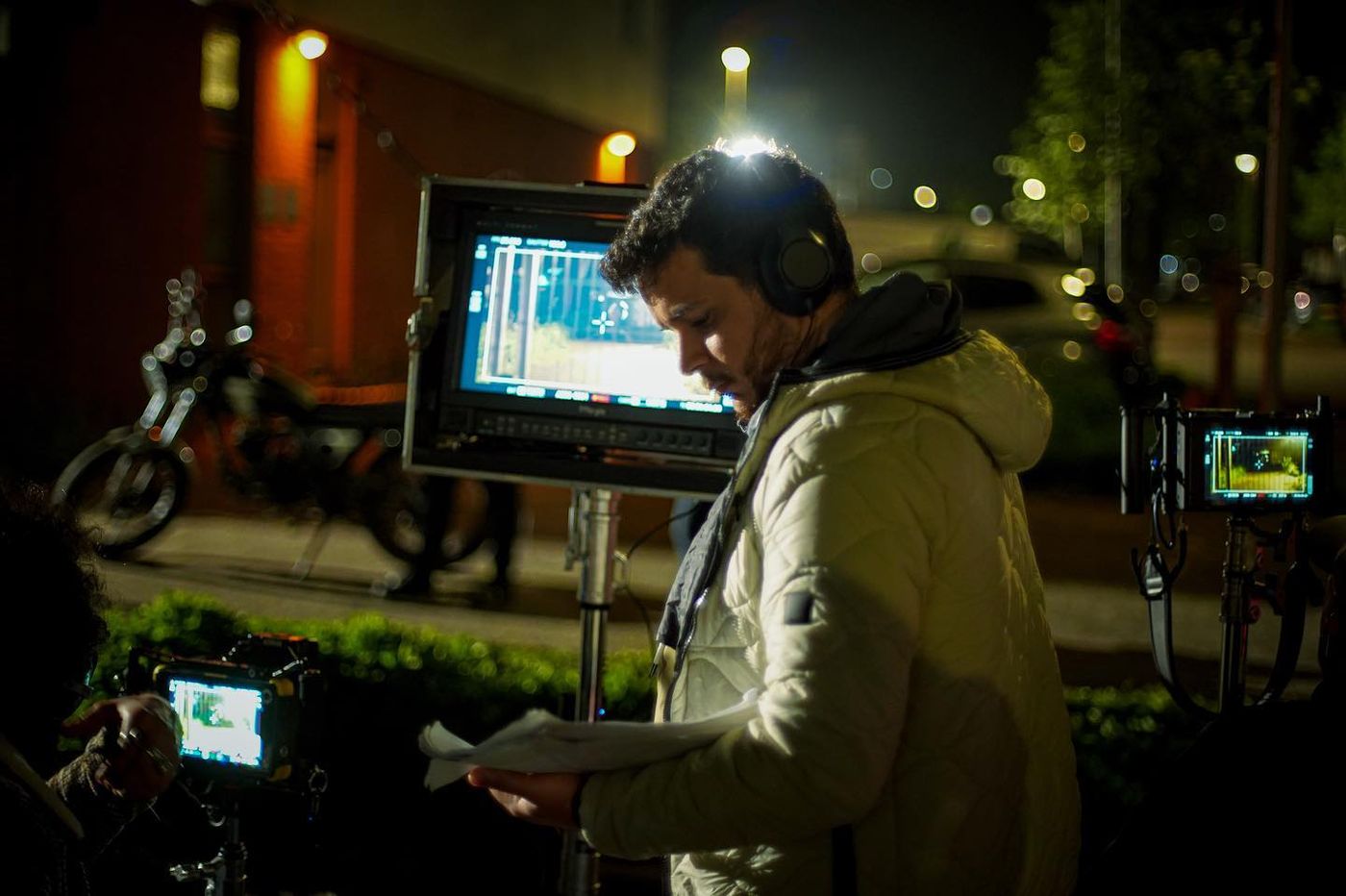 Mohammad Qahees looks down at papers beside production monitors during a nighttime film shoot.